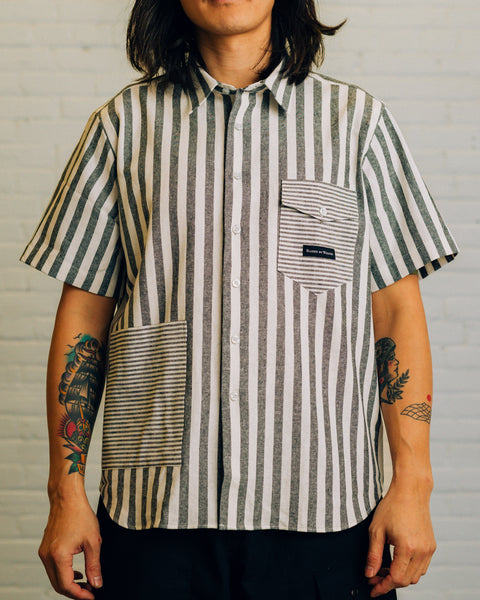 Front of a horizontal striped collar shirt with two pockets. Chest pocket has the Raised By Wolves logo in black.