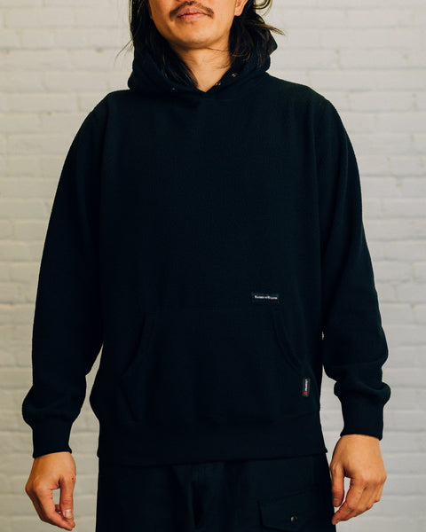 Front view of a black hoodie with two snap buttons at the neck. Near the pocket is the “Raised by Wolves” logo.