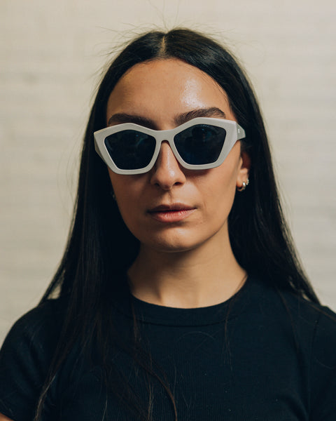 Front view of a woman wearing cement coloured oversized square sunglasses. And a side view with RBW inscribed in white. 