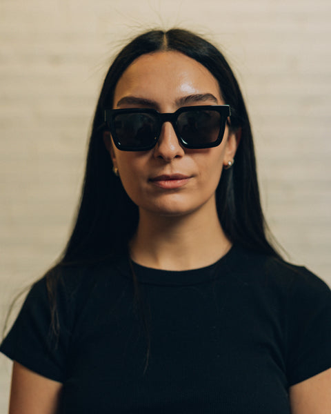 Front view of a woman wearing cement coloured geometric sunglasses. And a side view with RBW inscribed in white. 