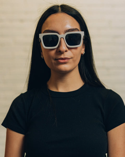 Front view of a woman wearing cement coloured geometric sunglasses. And a side view with RBW inscribed in white. 