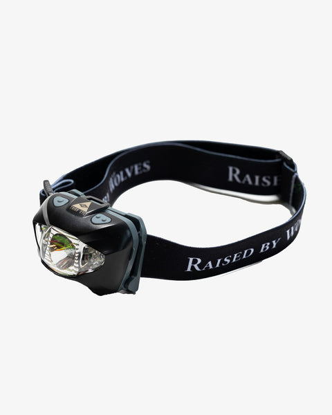 Black headlamp with a blue trim, and a third eye pendant on top of the light. The band is black and adjustable with Raised By Wolves printed around it in white. 