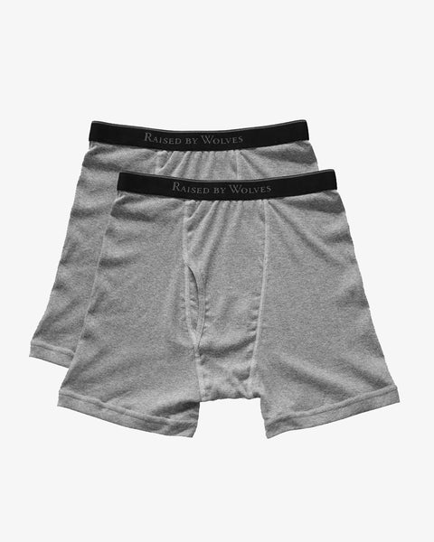 Two pairs of white cotton boxer briefs with a black band and Raised By Wolves printed in grey around the band.