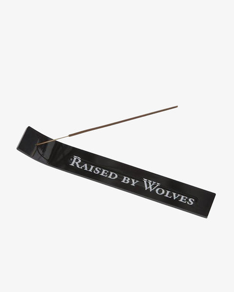 Black acrylic incense holder with the Raised By Wolves logo holding an incense stick.