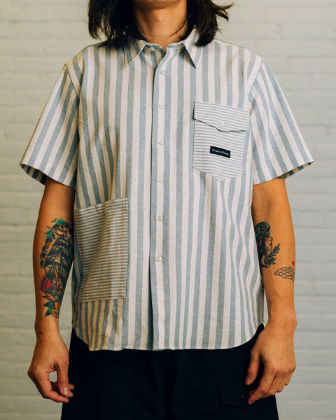 Front of a horizontal striped collar shirt with two pockets. Chest pocket has the Raised By Wolves logo in black.
