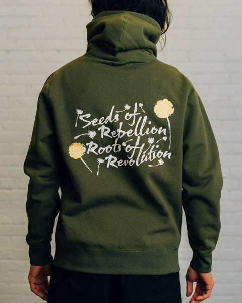 Back of an olive hoodie with script “Seeds of Rebellion Roots of Revolution” and yellow and white dandelions around it.