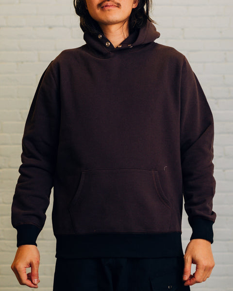 Front of a purple hoodie with two silver snap buttons at the neck. On the hood “Raised By Wolves” is embroidered in white.