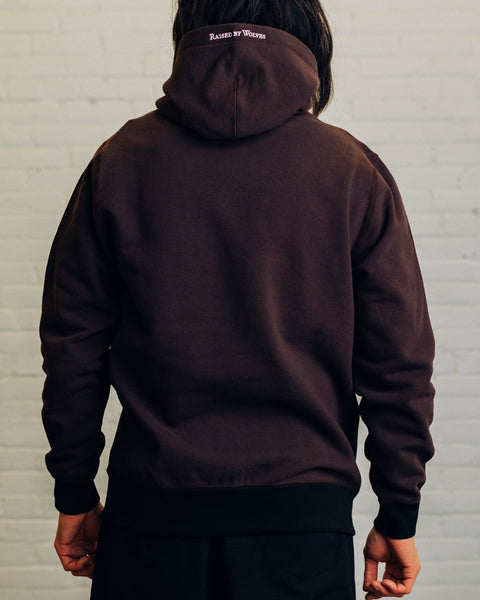 Front of a light grey hoodie with two snap buttons at the neck. On the hood “Raised By Wolves” is embroidered in white.