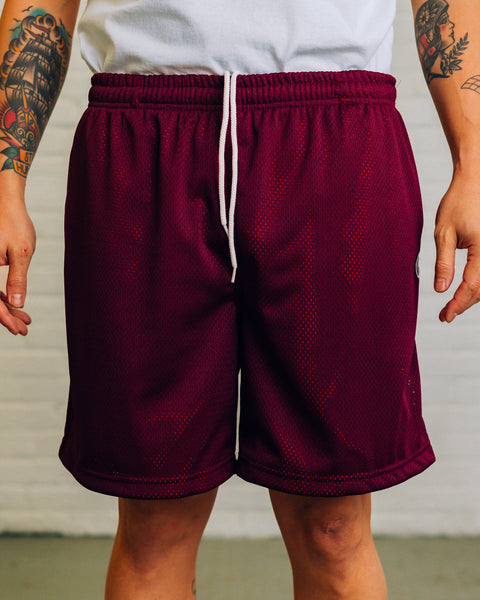 Front view of burgundy mesh overtop orange polyester shorts. The side view includes a small Raised By Wolves wolf logo.