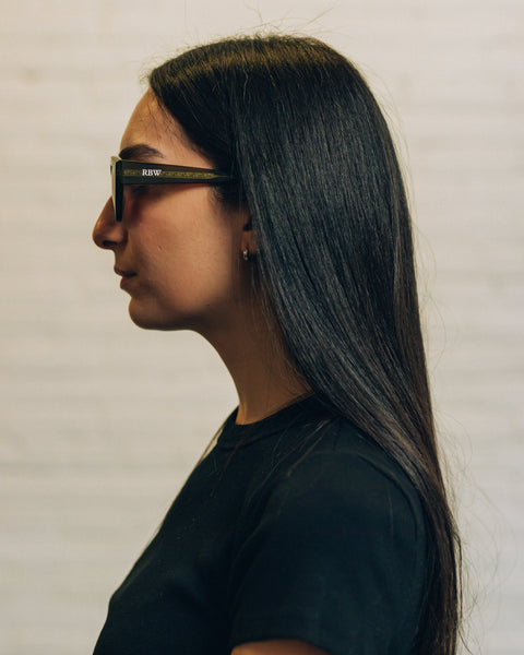 Front view of a woman wearing black oversized square sunglasses. And a side view with RBW inscribed in white. 